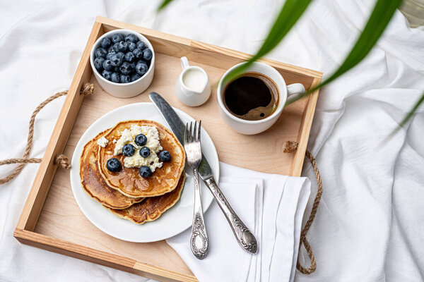 Sunday morning. Delicious breakfast of pancakes, berries and coffee on a wooden tray.