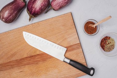 Taze patlıcanlar, baharatlar, mutfak bıçağı ve gri bir yüzey üzerindeki kesme tahtası..