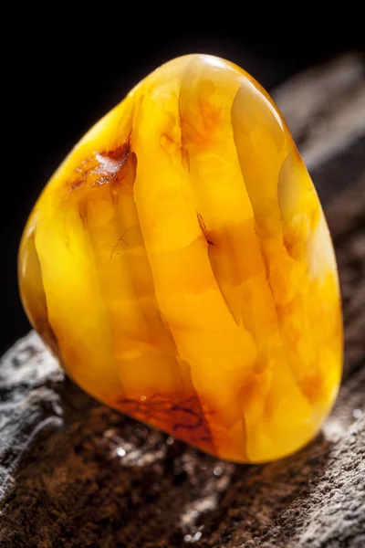 Natural amber. A piece of yellow opaque natural amber on large piece of dark stoned wood. — Stock Photo, Image