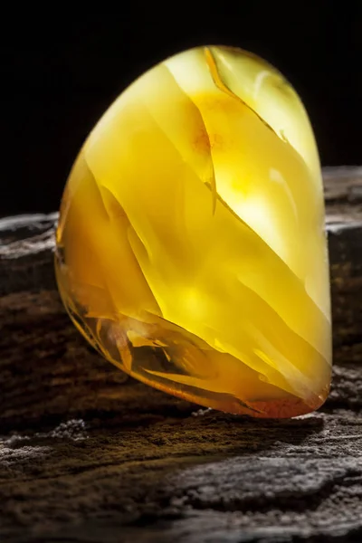 Natural amber. A piece of yellow opaque natural amber on large piece of dark stoned wood. — Stock Photo, Image