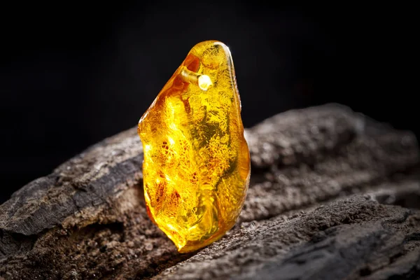 Естественный янтарь. Кусок желтого прозрачного натурального янтаря на большом куске темного камня . — стоковое фото