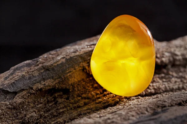 Natural amber. A piece of yellow opaque natural amber on large piece of dark stoned wood. — Stock Photo, Image