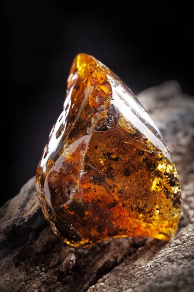 Natural amber stone. A piece of dirty transparent yellow amber on piece of stoned wood.