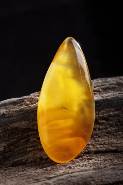 Natural amber. A piece of yellow opaque natural amber on large piece of dark stoned wood. — Stock Photo, Image