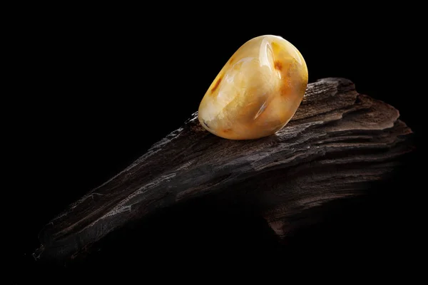 Ambra naturale. Un pezzo di giallo ambra naturale opaca su un grande pezzo di legno scuro lapidato . — Foto Stock