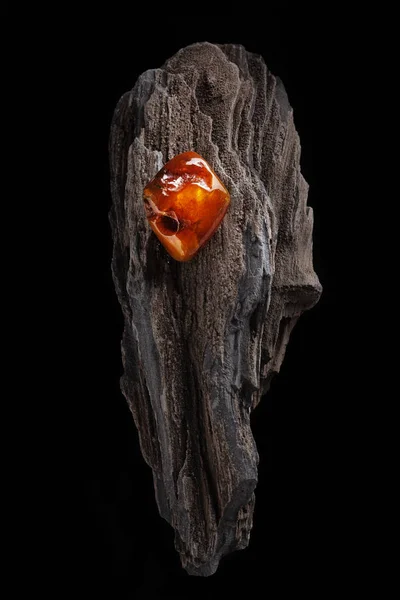 Natural amber. A piece of yellow and red semi transparent natural amber on piece of stoned wood. — Stock Photo, Image