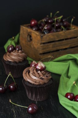 Vişne ve kiraz siyah bir zemin üzerine bir ahşap kutu ile lezzetli çikolata cupcakes