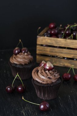 Vişne ve kiraz siyah bir zemin üzerine bir ahşap kutu ile lezzetli çikolata cupcakes