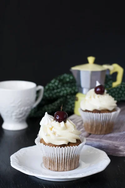 Vanilla cupcakes and chocolate cupcakes with cherries, cup and coffee pot on a dark background.