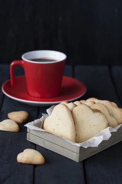 Tasty homemade gingerbread and coffee in a red cup on a black wooden background.