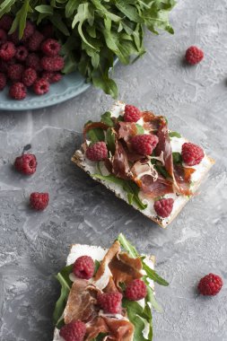 Bütün tahıl ekmeği, ev yapımı peynir, roka, jambon ve sulu ahududu sandviçle. Sağlıklı snack.