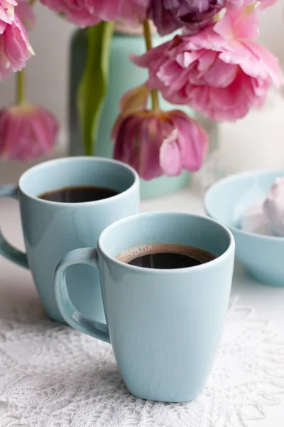 杯のブラック コーヒーと朝食の繊細なマシュマロが青い花瓶のピンクのチューリップの美しい花束の横にあります — ストック写真