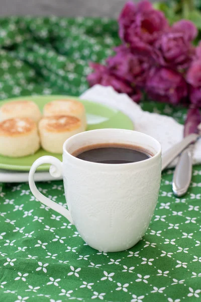 ホワイト洗練された一杯 朝食のための農家チーズの自家製からおいしい食事チーズケーキ 緑のテーブル クロスの上の紫のチューリップの花束ブラック コーヒー — ストック写真