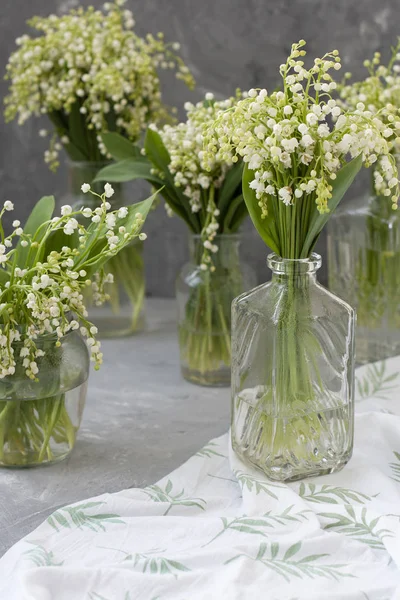 Wresh bouquets of lilies of the valley in glass vases on the whi