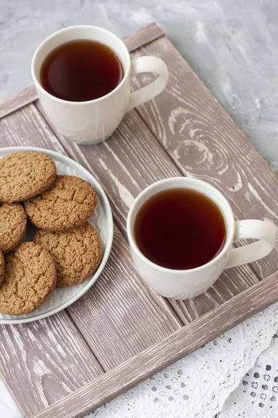 A tasty snack: two cups of tea and a plate of cookies.