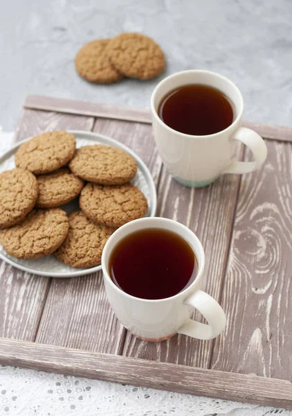 Een lekkere snack: twee kopjes thee en een bord koekjes. — Stockfoto