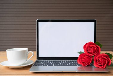 Ahşap arka planda dizüstü bilgisayarı olan kırmızı gül ve kahve fincanı, Sevgililer Günü konsepti
