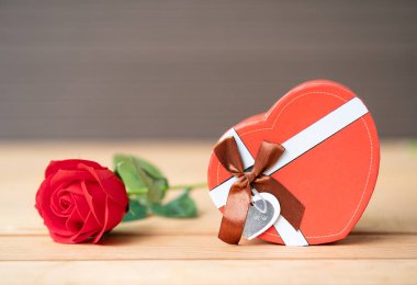 Kırmızı gülleri ve ahşap arka plandaki kalp şeklindeki kutuyu, güllü sevgililer günü konseptini ve kırmızı kalp şeklindeki kutuyu kapat.