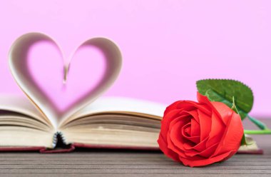 Kitabın sayfaları kalp şeklinde kıvrılmış ve kırmızı gül şeklinde. Pembe arka plandaki kitap sayfalarından kalp şekli kavramı