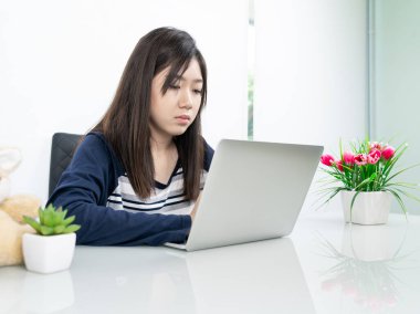 Oturma odasında oturan genç kız öğrenci bilgisayarla internetten öğreniyor.
