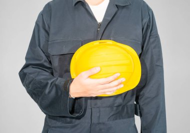 Gri arka planda izole edilmiş sarı baret tutan mavi kapaklı işçiler giyiniyor.