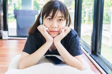 Kulaklıklı genç bir kız ve evde cep telefonundan müzik dinliyor.