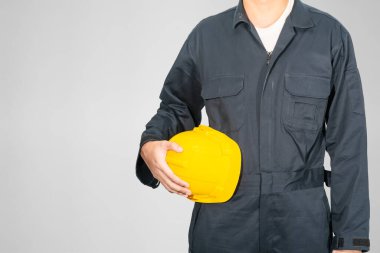 Gri arka planda izole edilmiş sarı baret tutan mavi kapaklı işçiler giyiniyor.