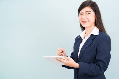 Takım elbiseli Asyalı genç kız mavi arka planda bilgisayar tableti kullanıyor.