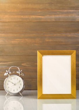 Resim, ahşap arka planlı masa üzerinde altın çerçeve ve çalar saat ile taklit