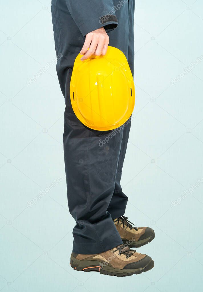 Worker standing in blue coverall holding yellow hardhat isolated on blue background