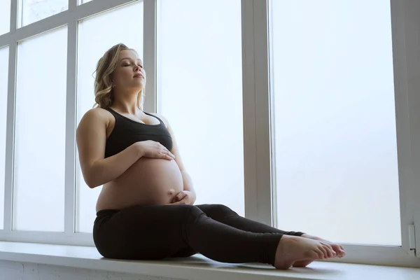 Молодая беременная блондинка занимается фитнесом на подоконнике — стоковое фото