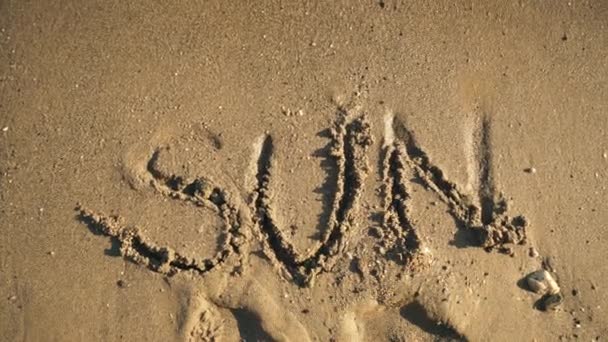 Λέξη «ήλιος» πάνω στην άμμο βρέχεται από τα κύματα βίντεο — Αρχείο Βίντεο