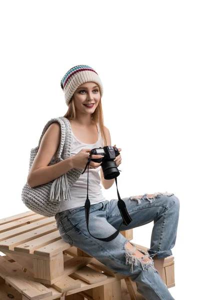 Charming smiling young woman in hat with photo camera and handbag on pallets — Stock Photo, Image