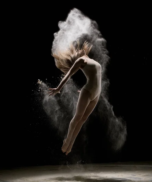 Slim girl jumping in white dust in the dark — Stock Photo, Image