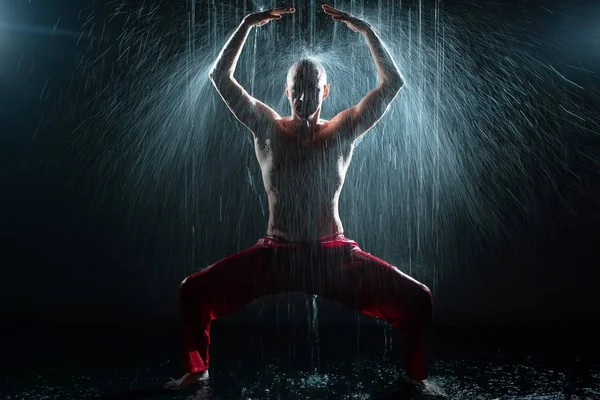Мужчина без рубашки занимается гимнастикой под дождем — стоковое фото