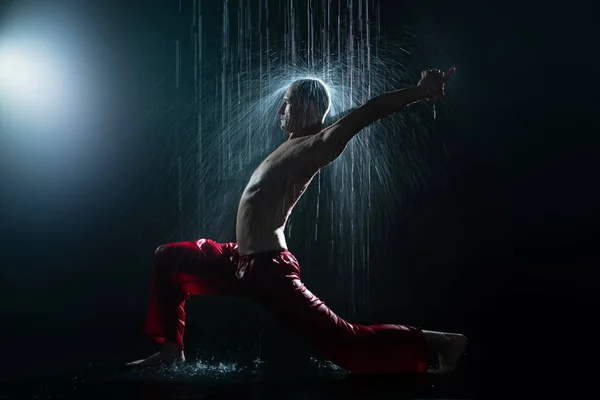 Un hombre sin camisa haciendo yoga bajo la lluvia — Foto de Stock