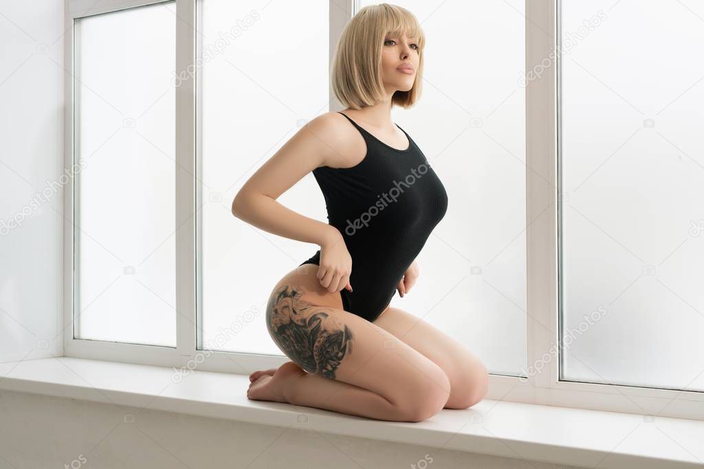 Tattoed blonde in black body on window sill