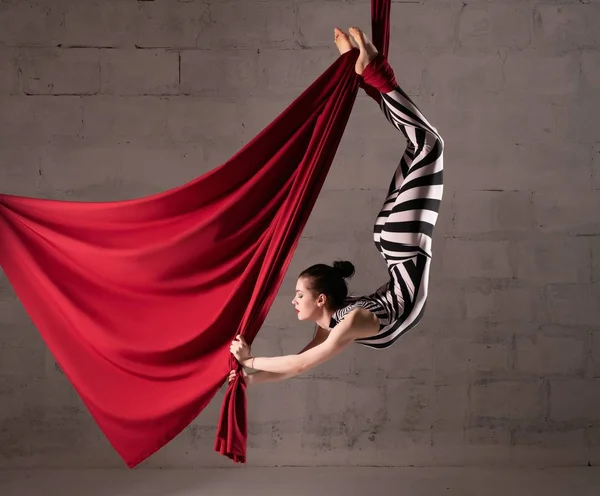 Young gymnast hanging on red cloth — Stock Photo, Image