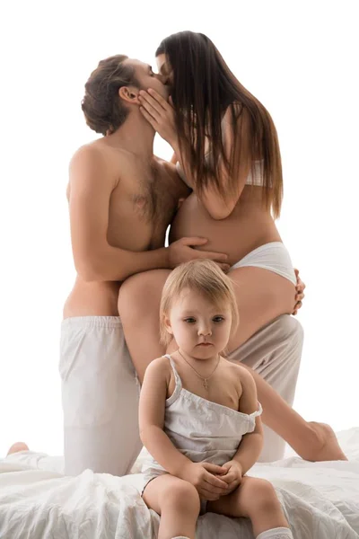 Baby sitting near kissing parents — Stock Photo, Image