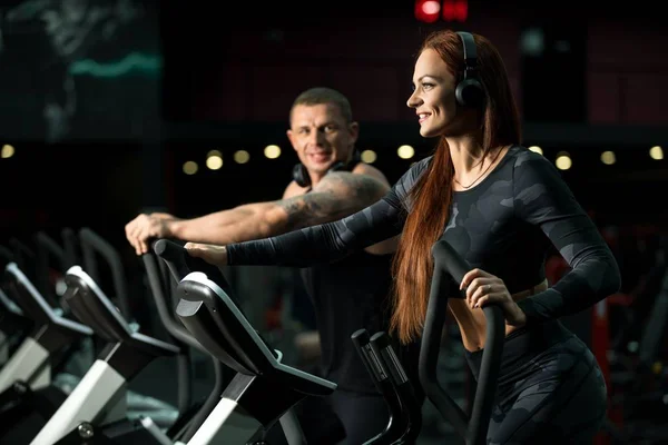 Hombre y mujer haciendo ejercicio sobre simuladores en un gimnasio — Foto de Stock