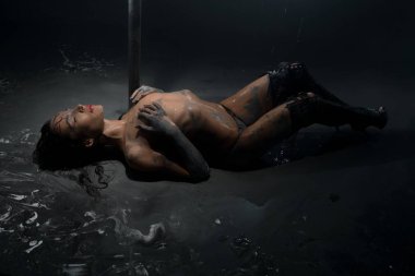 Esmer üstsüz çamur görünümünde yerde yatıyor