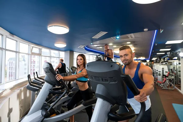 Joven hermosa pareja en simuladores en un gimnasio — Foto de Stock