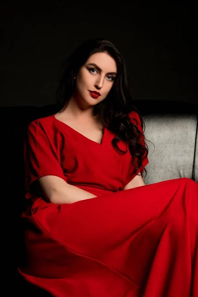 Sexy brunette in red sitting on the sofa — Stock Photo, Image