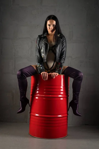 性感的女孩在夹克坐在铁桶拍摄 — 图库照片