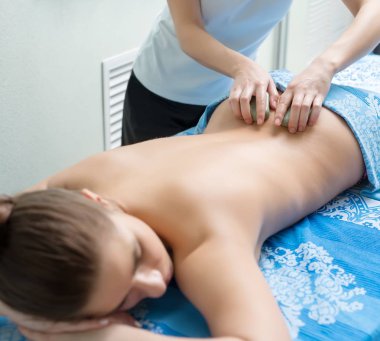 Genç bir kadın kaplıca salonunda sıcak taş masajı yaptırıyor.