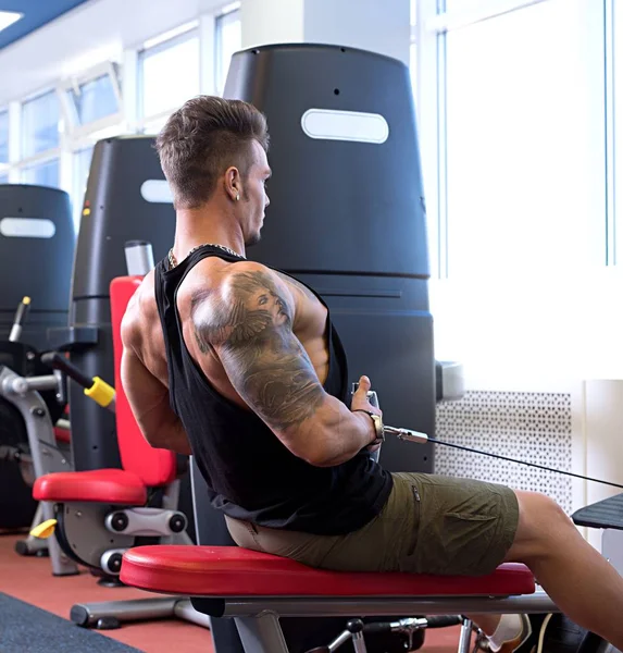 Im Fitnessstudio. Tätowierter Bodybuilder trainiert im Simulator — Stockfoto