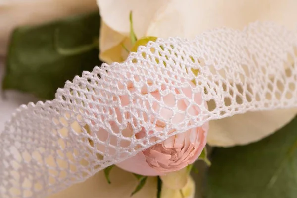 White lace ribbon on the table among roses shot — Stock Photo, Image