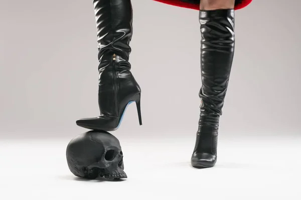 Crop woman in boots stepping on human skull