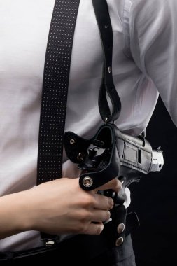 Pantolon askısı ve omuz kılıfı olan beyaz bir gömlek giyen bir adamın eli kılıfının içindeki tabancanın yanında..