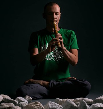 Yogada oturan bir adam stüdyonun yanında beyaz taşlarla poz veriyor.